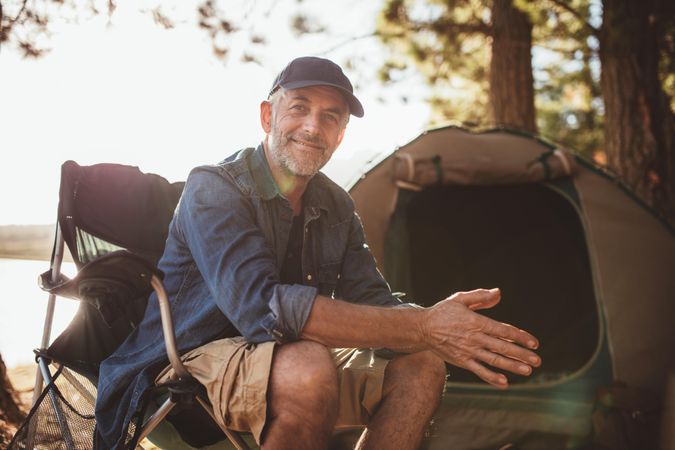 Portrait of a happy mature man sitting in front of a tent and looking at camera