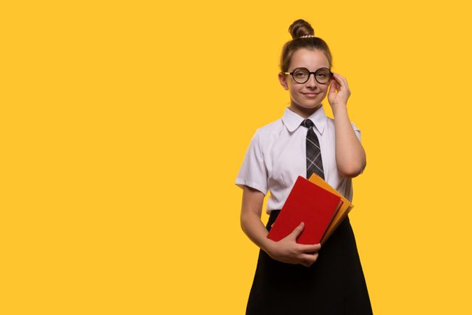 Teen girl adjusting glasses, holding books, wearing school uniform