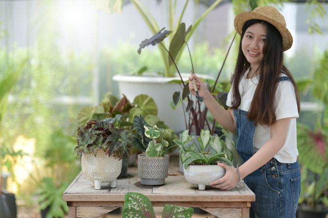 Smiling Asian female in a green house working with plants on a table