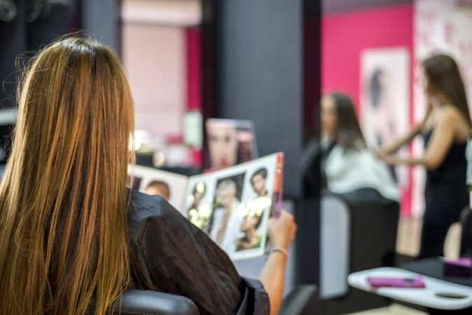 Back of woman with long hair sitting in salon chair with hair magazine