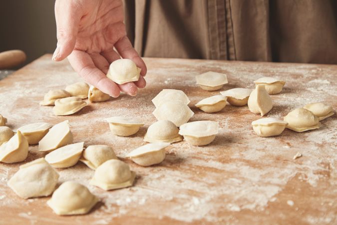 Fresh ravioli on bread board with hand holding one