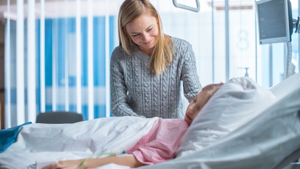 Cute Little Girl Sleeps on a Bed in the Children's Hospital, Caring Mother Covers Her with a Blanket and Caresses Her Forehead