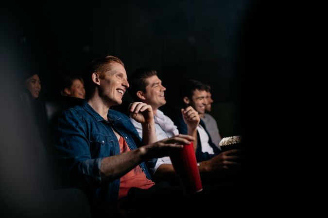 Smiling young man with friends in cinema hall watching movie