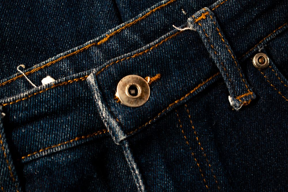 Close up gold and shiny button navy blue jeans fabric background texture.