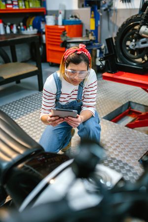 Mechanic with security glasses and digital tablet review motorcycle on garage