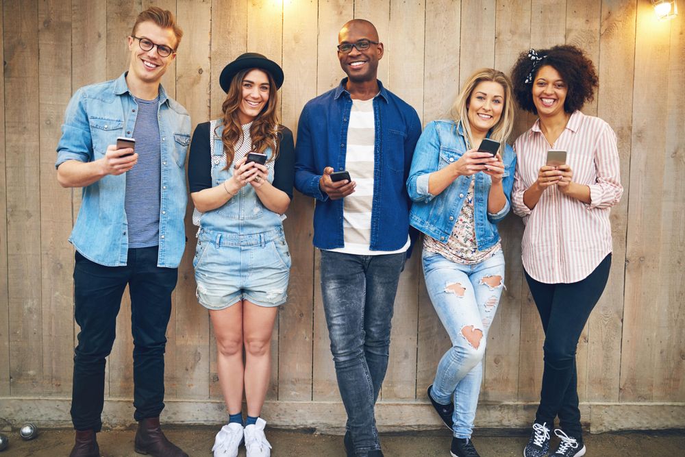 Multi-ethnic group of friends standing against a wooden fence smiling at the camera