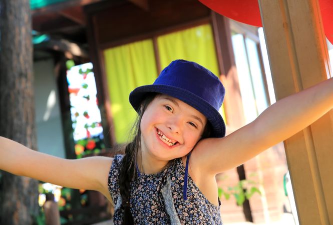 Portrait of happy little girl wearing a blue hat with her arms outstretched