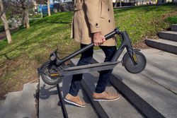 Crop man carrying folded electric scooter in city