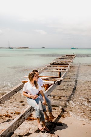 Glad lovers cuddling on destroyed pier on seashore
