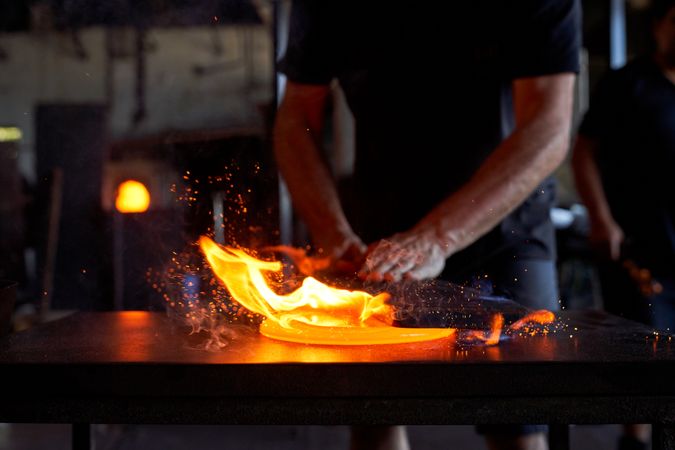 Crop craftsman making glass product in glassblowing workshop