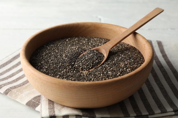 Wooden bowl with chia and spoon on wooden background, space for text