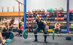 Woman screaming at weightlifting failure while her gym mates cheer her on