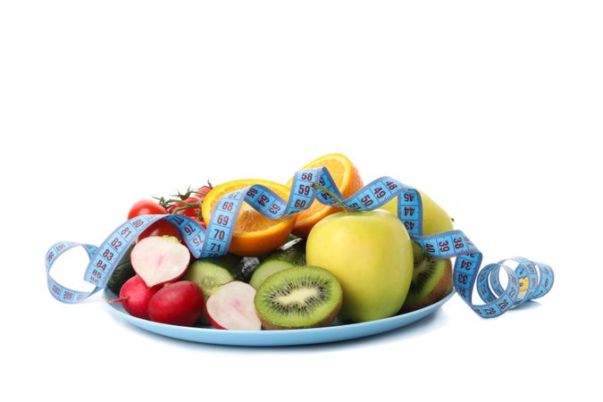 Plate with measuring tape and vegetarian food isolated on light background