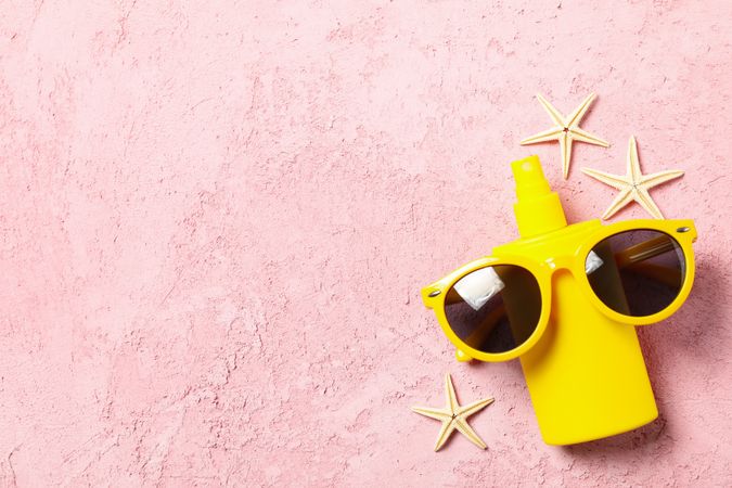 Sunscreen, sunglasses and starfishes on pink background