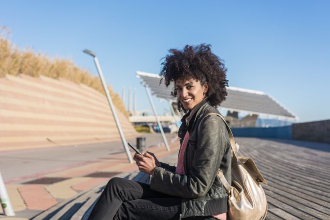 Black woman with afro hair sitting on the street with her smartp
