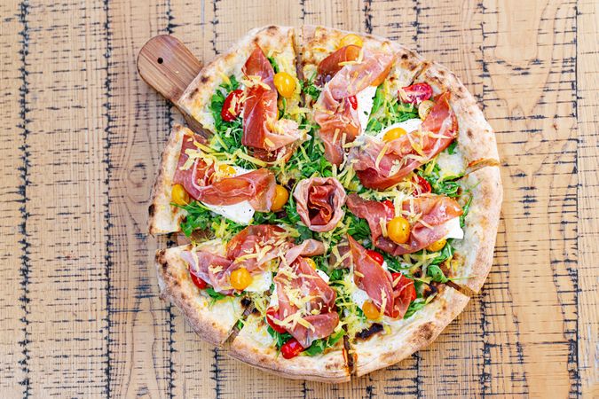 Gourmet Italian Pizza with Prosciutto, Arugula, and Colorful Cherry Tomatoes on Rustic Wooden Board