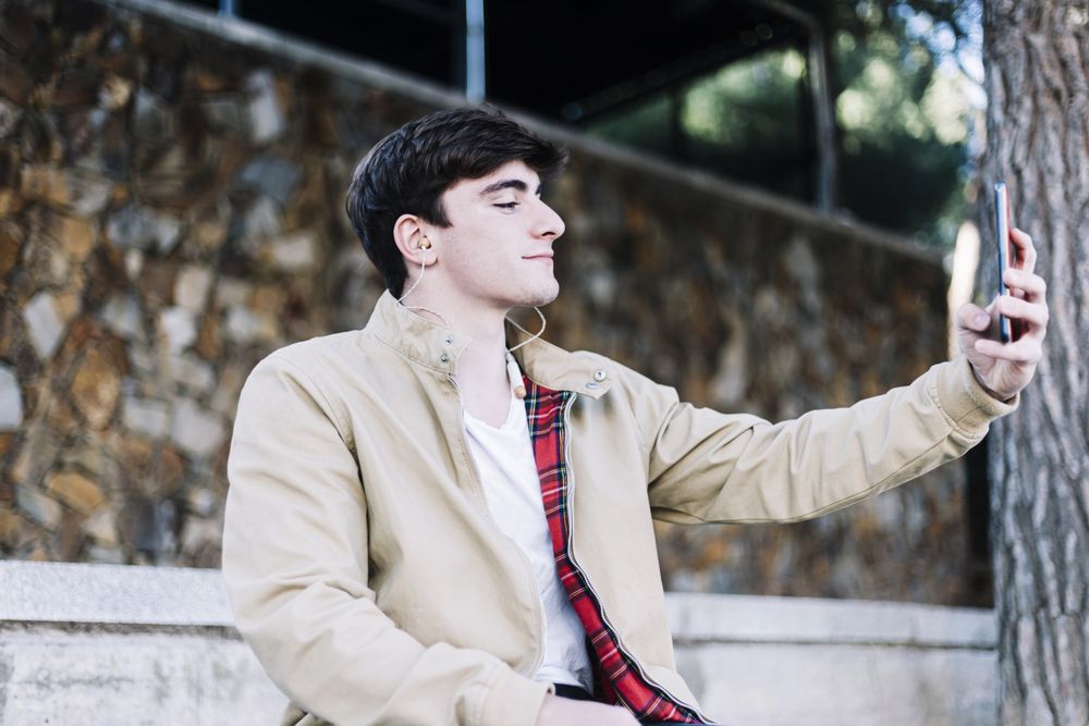 Man sitting outdoors taking selfie with smartphone