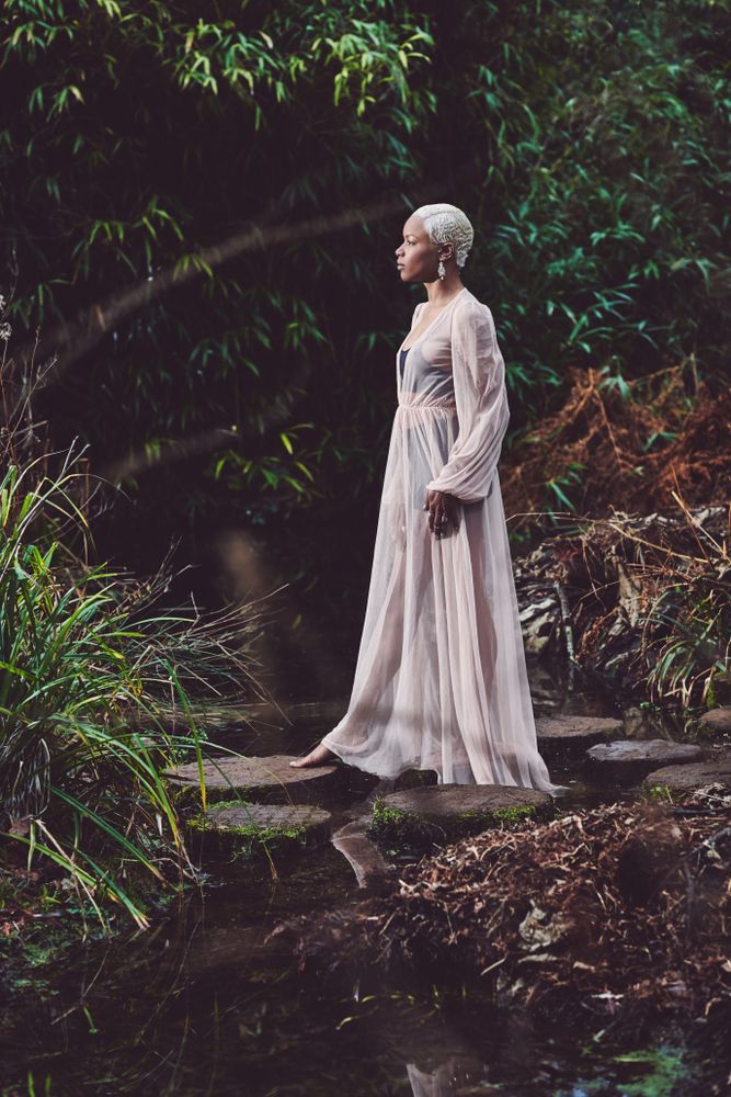 Woman in mesh dress stepping onto rocks on pond