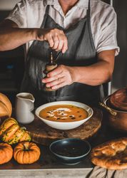 Woman grinding pepper onto soup in cozy kitchen, close up
