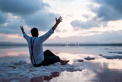 Relaxed man standing with outstretched hands with empty fish tank at shore