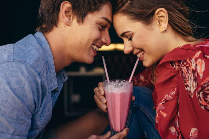 Close up of a happy couple sharing a milkshake with two straws