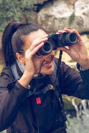 Smiling woman tourist with backpack looking at binoculars