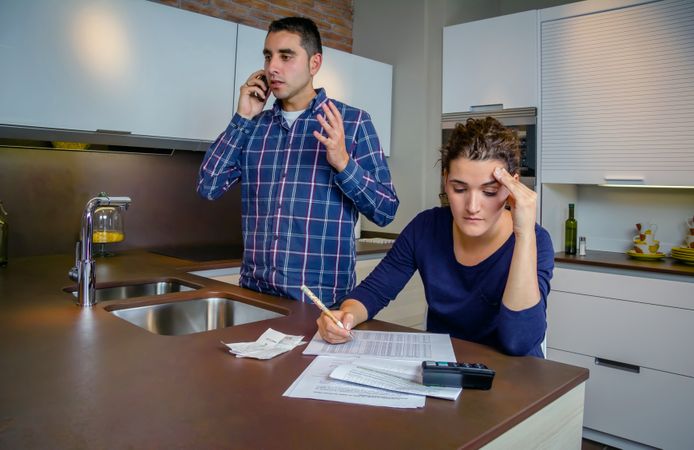Man making phone call as woman works on bills in kitchen counter