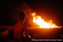 Back of young boy watching fire in field at night 5qmyo5
