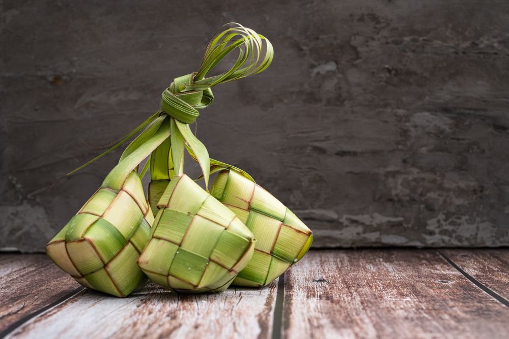Uncooked ketupat filled with rice, placed on wooden surface