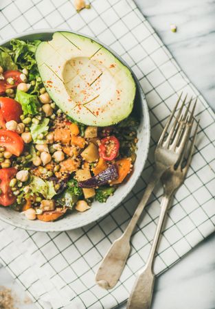Healthy vegan lunch bowl with avocado, sprouted grains, vegetables, with forks on checkered napkin