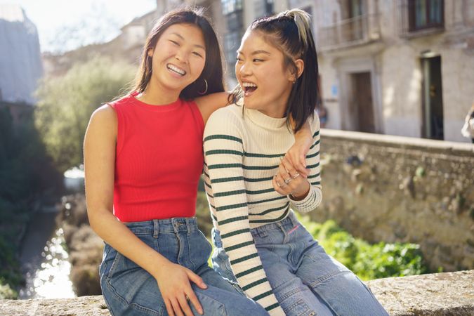 Cheerful female friends sitting outside on sunny day