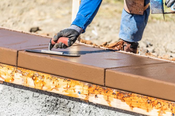 Construction Worker Using Trowel On Wet Cement Forming Coping Around New Pool