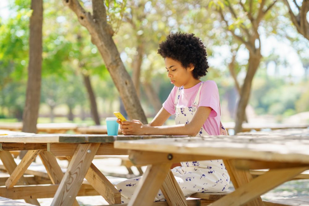 Serious woman sitting on park table texting