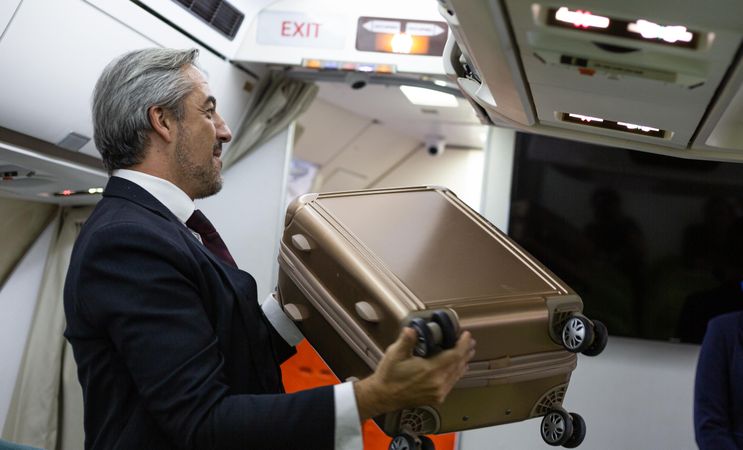 Male in business attire putting small suitcase above seats in storage
