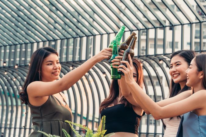 Group of happy Asian female friends celebrating by toasting drinks on rooftop