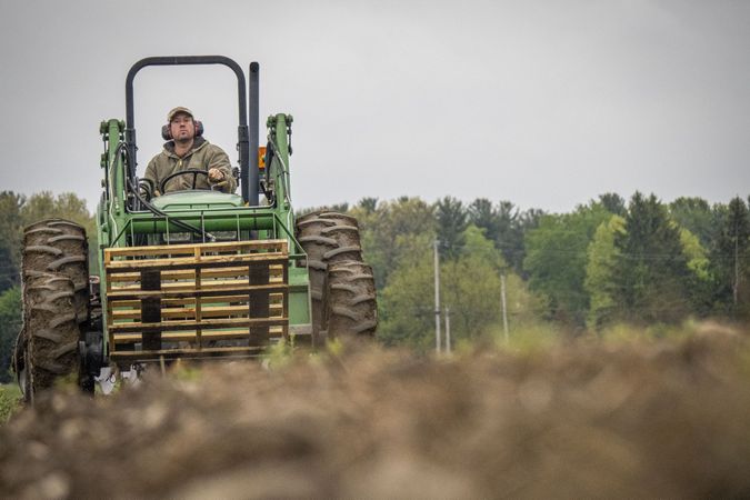 Copake, New York - May 19, 2022: Man on tractor in muddy field, copy space