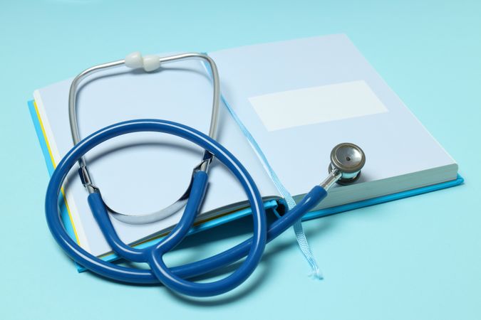 Notepad and stethoscope on blue background, close up