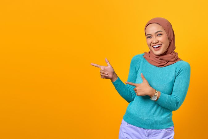 Smiling Muslim woman pointing at copy space