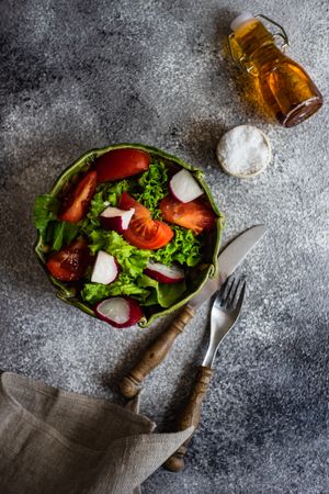 Top view of salad with tomatoes, radish & lettuce on concrete background served with olive oil and salt