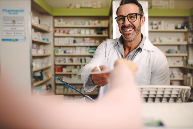 Male pharmacist taking prescription from customer at pharmacy