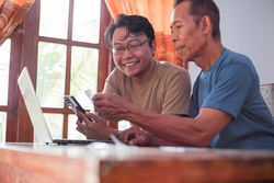 Happy adult son and mature father pay online using laptop and credit card