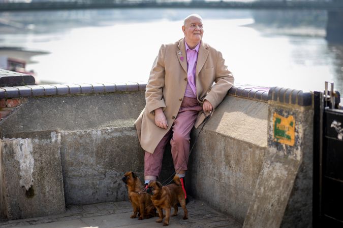 Man in purple button-down standing by river with two dogs