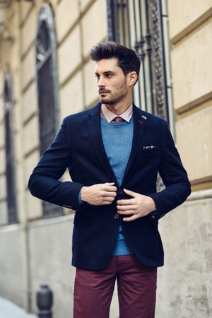 Attractive man in the street wearing elegant suit looking to side fixing buttons