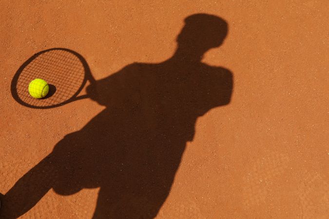 Shadow of female tennis player on clay court with ball
