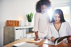 Two female colleagues, one sitting, one standing going over images for work