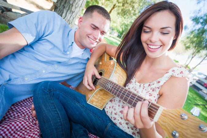 Adult Female Playing Guitar with Boyfriend In The Park.