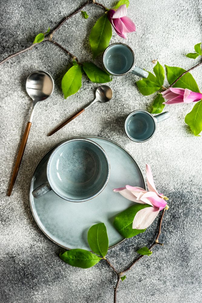 Top view of cups & plate with magnolia flowers on grey counter