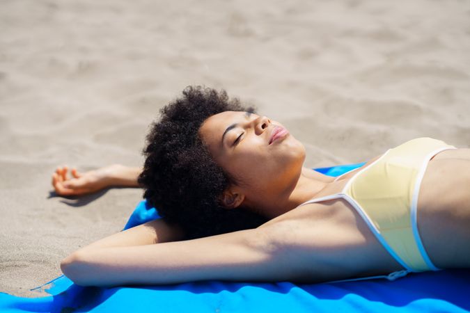 Female in yellow bikini relaxing on blue towel on the sandy beach