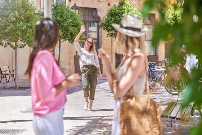 Young woman waving hand to friends in street