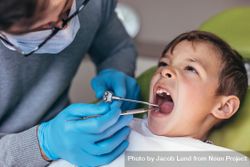 Pediatric dentist examining teeth of boy patient in dental clinic using dental tools 4daPLb
